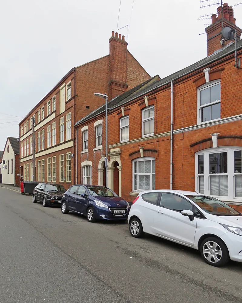 The red-brick John Lobb Westminster Works factory building on a terraced Northampton street, with cars parked outside